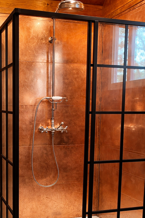 Shower enclosure with copper walls and black-framed glass doors.
