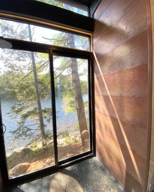 Window view of a forest and lake with copper wall panels.