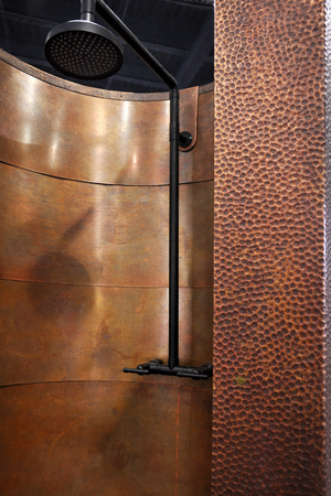 Copper shower enclosure with a black shower head against a textured brown wall.